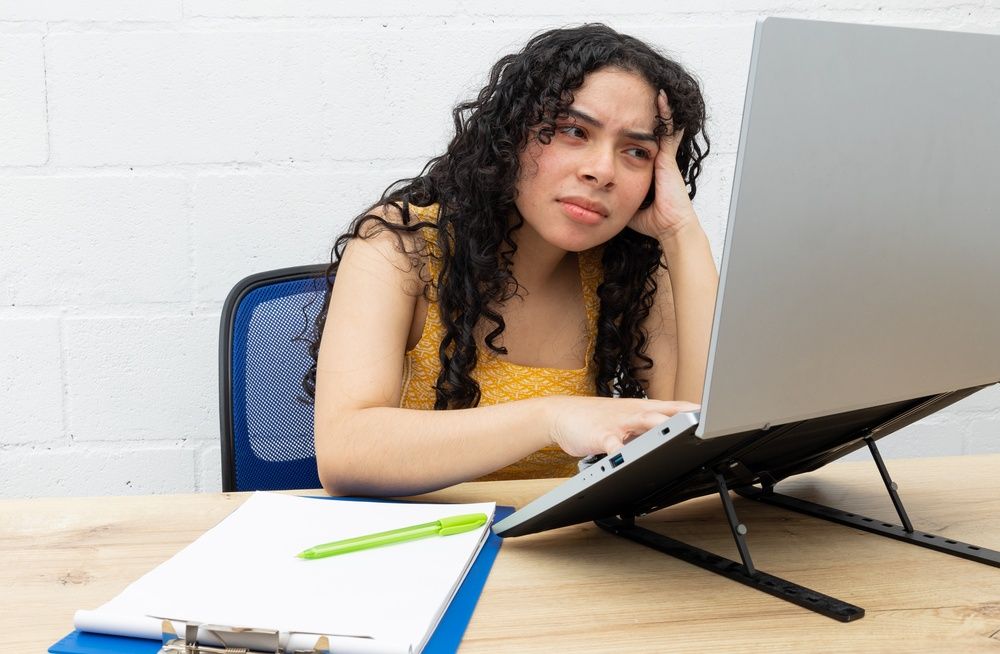 An image of a woman looking confused while using a laptop at a desk