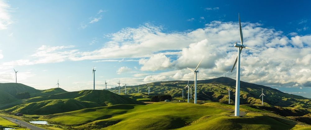 An image of a hilly landcsape in bright sunshine with a wind farm on the land